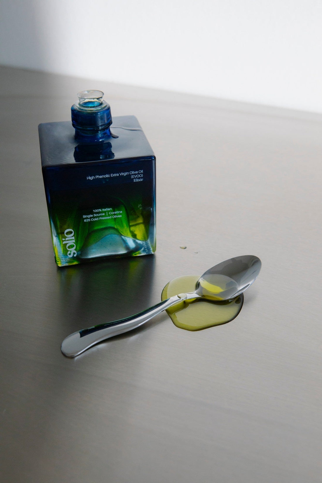 Solio Flasche neben einem Löffel mit Olivenöl auf Edelstahl